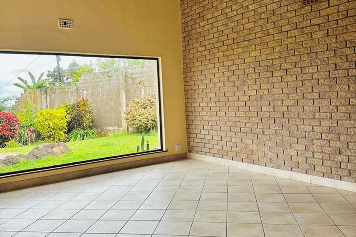 Spacious living area featuring a high exposed timber beam ceiling, a prominent feature brick wall, and large windows overlooking the garden.