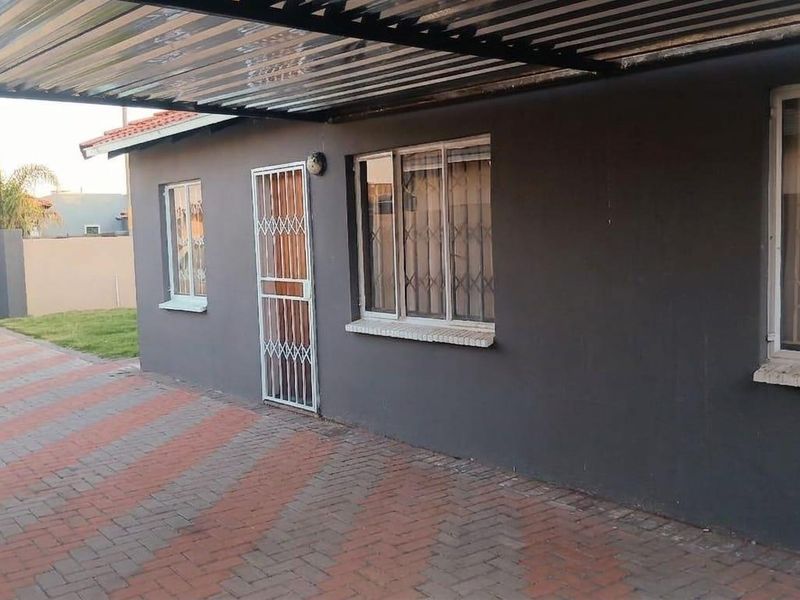 Front exterior view featuring a paved driveway, covered carport, and secure windows with burglar bars.