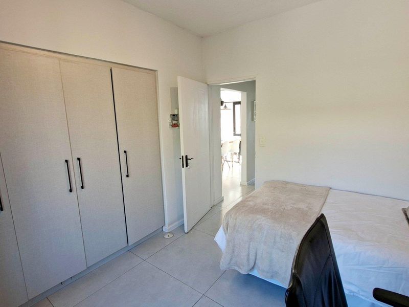 A well-maintained bedroom featuring neutral tiled flooring and ample built-in cupboard storage, with direct access to the adjacent living area.