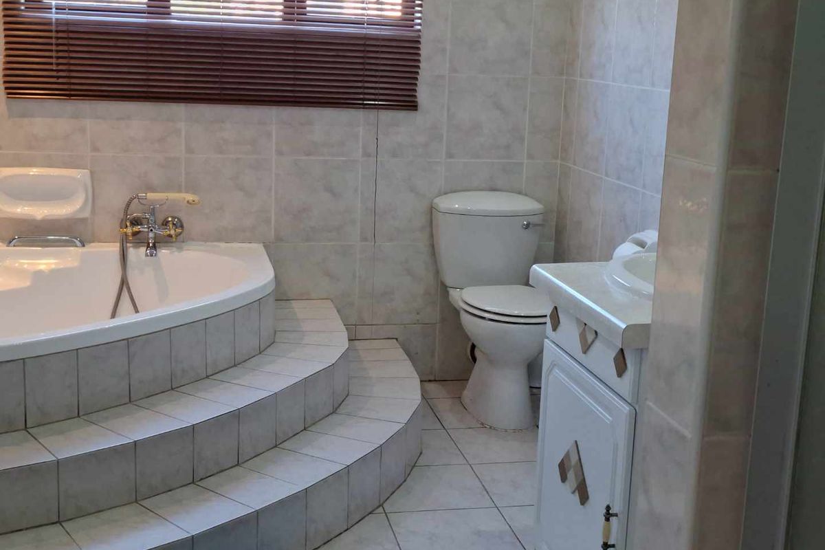 A functional bathroom featuring a raised corner bathtub with tiled steps, a standard toilet, and a vanity basin with built-in cabinetry.