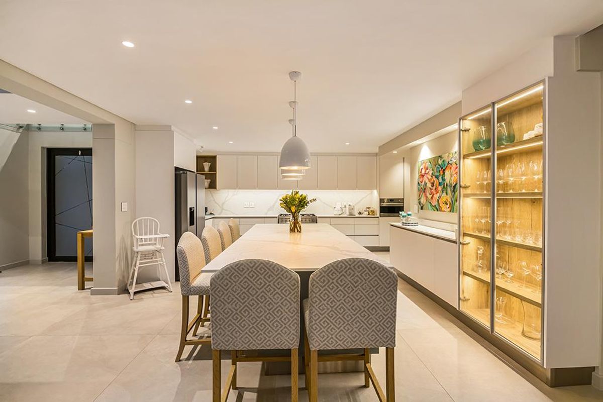 Modern open-plan kitchen featuring a large central island with stone countertop, integrated cabinetry, recessed lighting, and a built-in illuminated display cabinet.