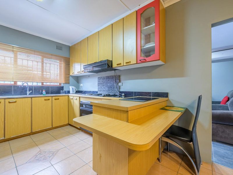 A functional kitchen featuring light wood-tone cabinetry, a built-in oven with extractor fan, tiled splashbacks, and an integrated breakfast nook.