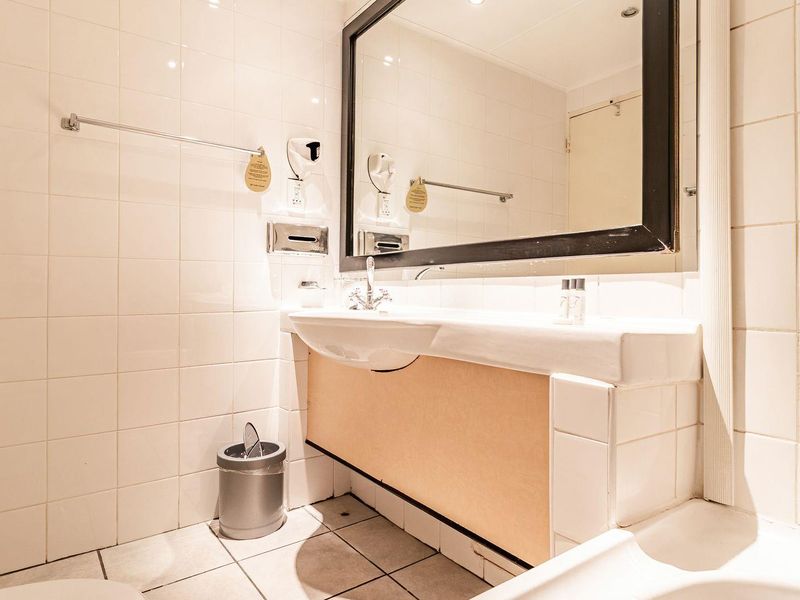 A functional bathroom featuring a wall-mounted basin, large vanity mirror, and bathtub with tiled finishes throughout.