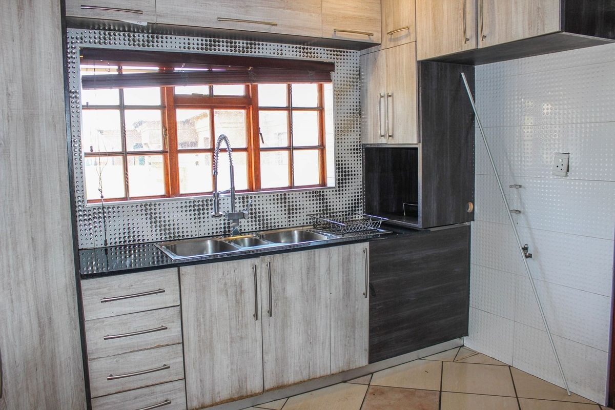 A kitchen area featuring built-in cabinetry, a double sink with a gooseneck tap, and tiled splashbacks, currently requiring minor repairs to cabinetry and fixtures.