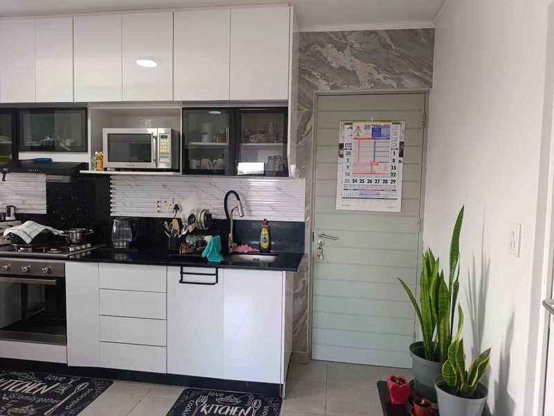 Modern kitchen featuring white high-gloss cabinetry, black granite countertops, integrated appliances, and a stylish marble-effect feature wall near the doorway.