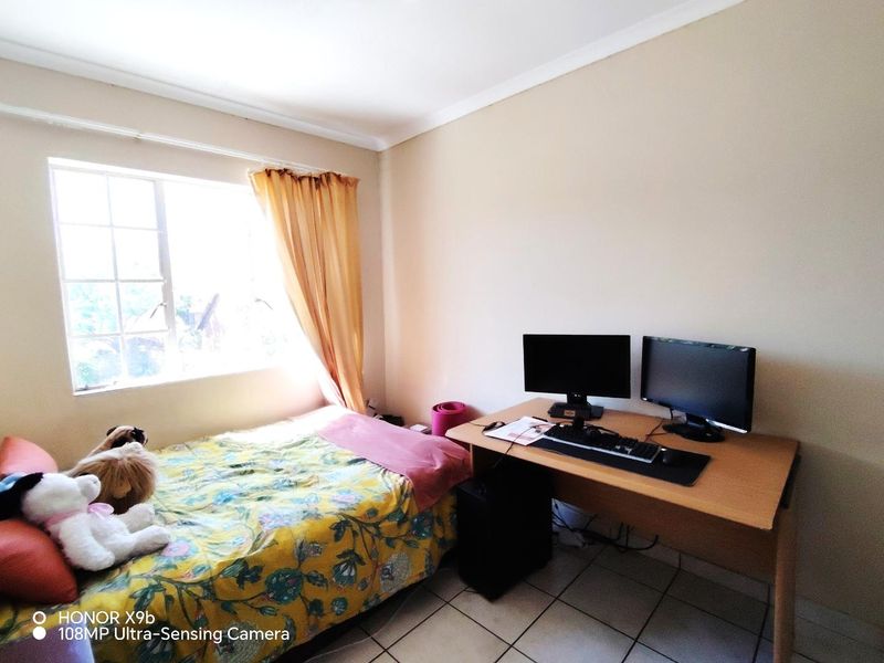 A functional bedroom featuring tiled flooring and a window with security bars, suitable for use as a sleeping area or home office.