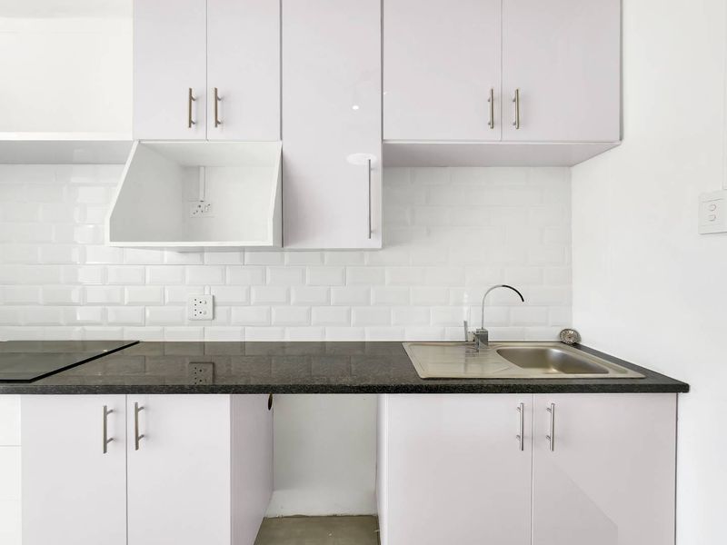A clean, modern kitchen featuring white gloss cabinetry, a subway tile backsplash, granite countertops, and a stainless steel sink.