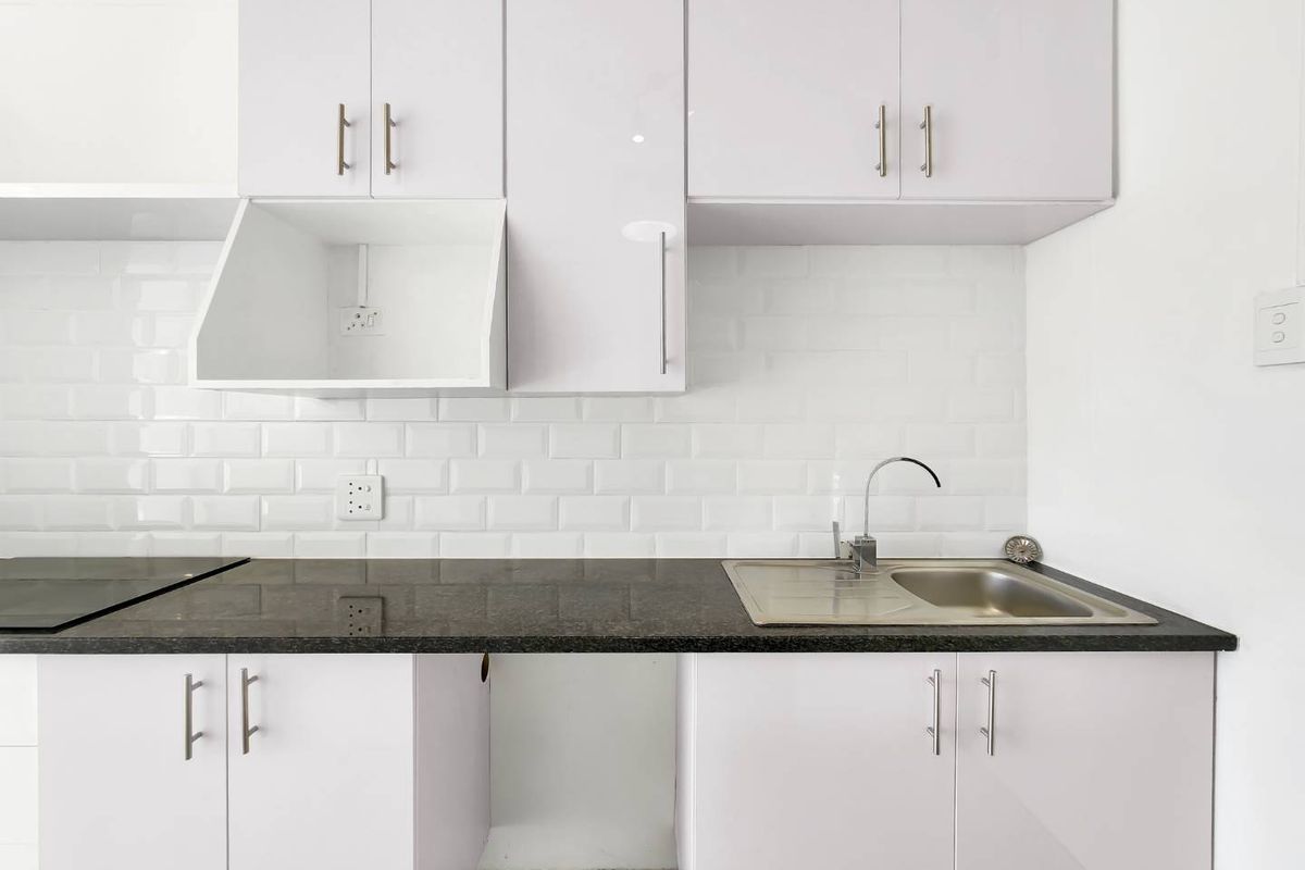 A clean, modern kitchen featuring white gloss cabinetry, a subway tile backsplash, granite countertops, and a stainless steel sink.