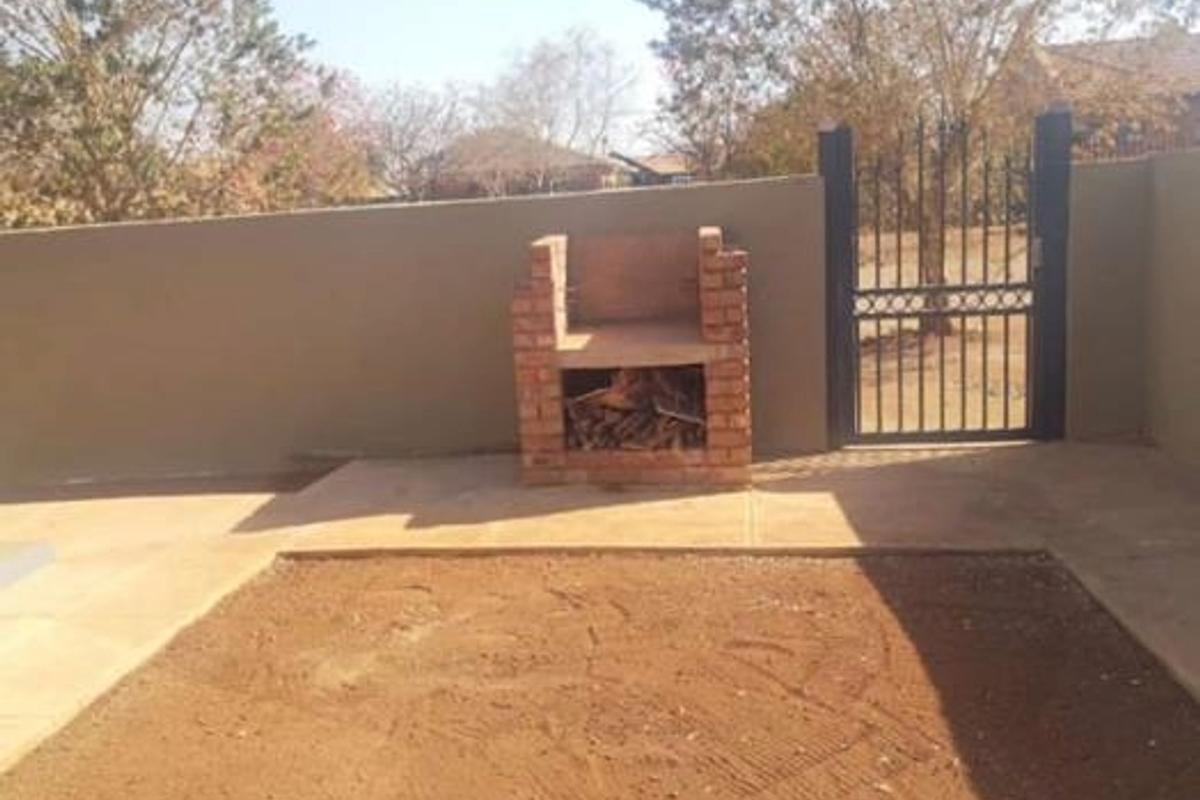 Outdoor area featuring a built-in brick braai and a metal security gate, set against a perimeter wall with an unfinished garden space.