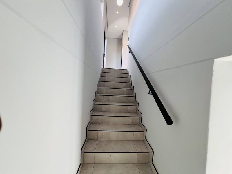 A modern, well-lit staircase featuring tiled steps and a sleek black handrail, providing clean and contemporary access between levels.