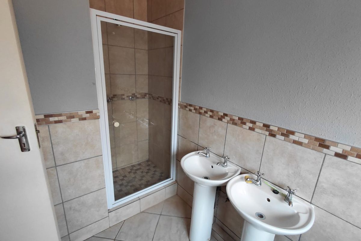 A functional bathroom featuring dual pedestal wash basins and a separate shower enclosure with tiled finishes and a decorative mosaic border.