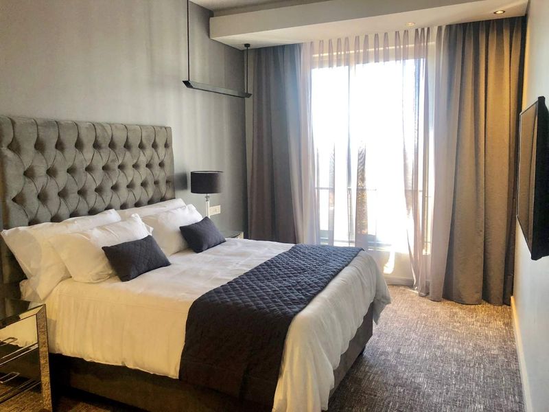A well-maintained bedroom featuring a tufted headboard, recessed ceiling lighting, and a large sliding glass door providing access to a balcony.