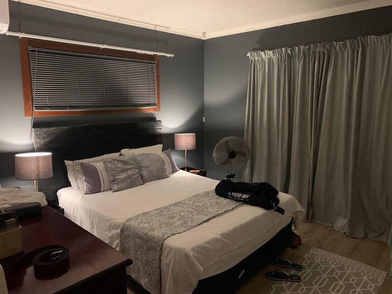 A cozy bedroom featuring dark painted walls, timber-framed windows with venetian blinds, and neutral laminate flooring.