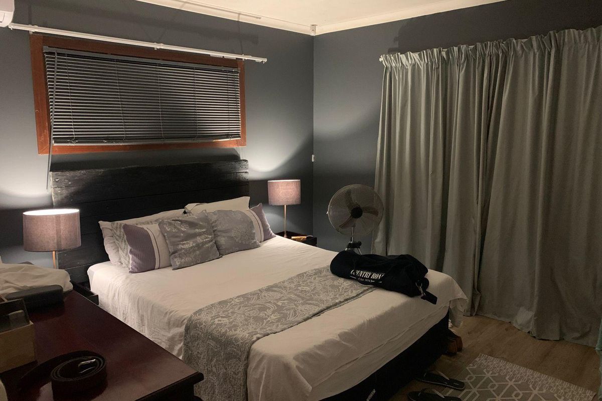 A cozy bedroom featuring dark painted walls, timber-framed windows with venetian blinds, and neutral laminate flooring.