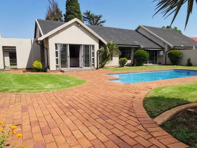 A well-maintained rear garden featuring a swimming pool, paved patio area, and a traditional thatched lapa, perfect for outdoor entertaining.