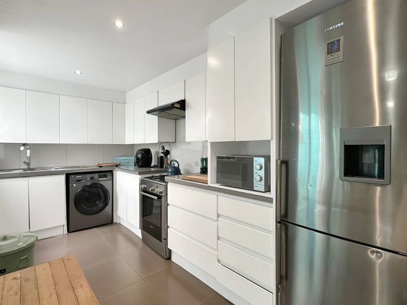 Modern kitchen featuring white cabinetry, stainless steel appliances, gas cooktop, extractor fan, and tiled flooring with integrated laundry facilities.