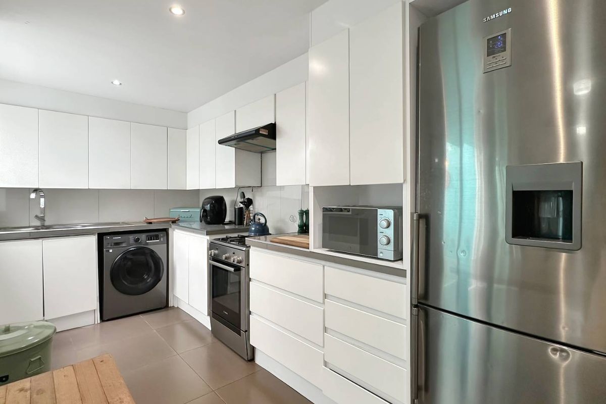 Modern kitchen featuring white cabinetry, stainless steel appliances, gas cooktop, extractor fan, and tiled flooring with integrated laundry facilities.