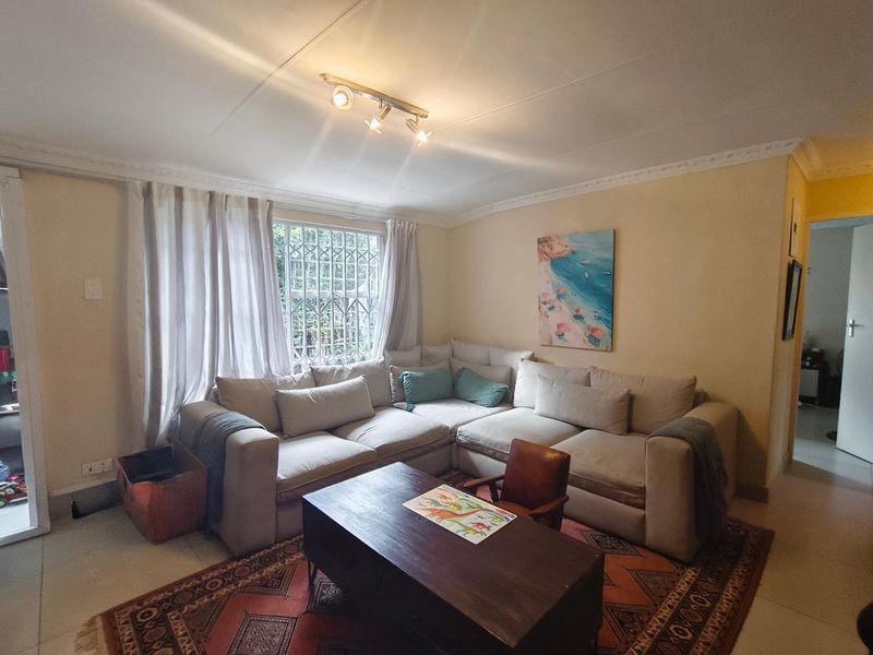 A comfortable living room featuring tiled flooring, ceiling cornice detailing, and a window fitted with a security gate.