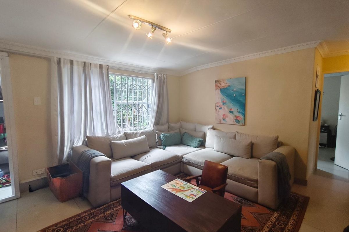 A comfortable living room featuring tiled flooring, ceiling cornice detailing, and a window fitted with a security gate.