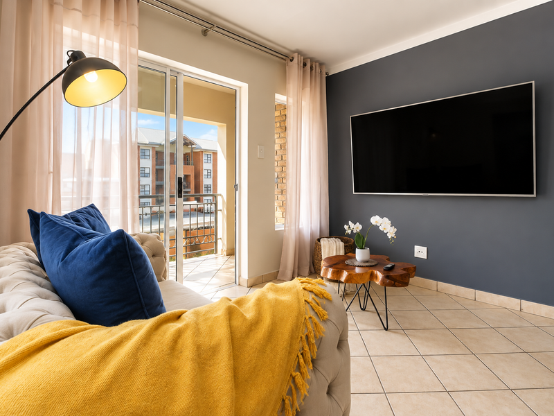 A bright living room featuring tiled flooring, a dark accent wall, and a sliding glass door providing access to a private balcony.