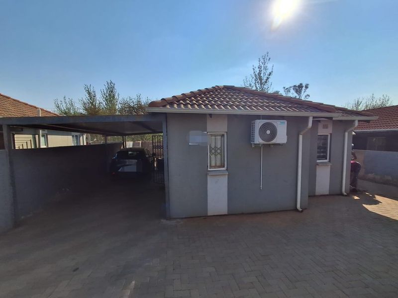Front exterior view of the house featuring a paved driveway, attached carport, and wall-mounted air conditioning unit.
