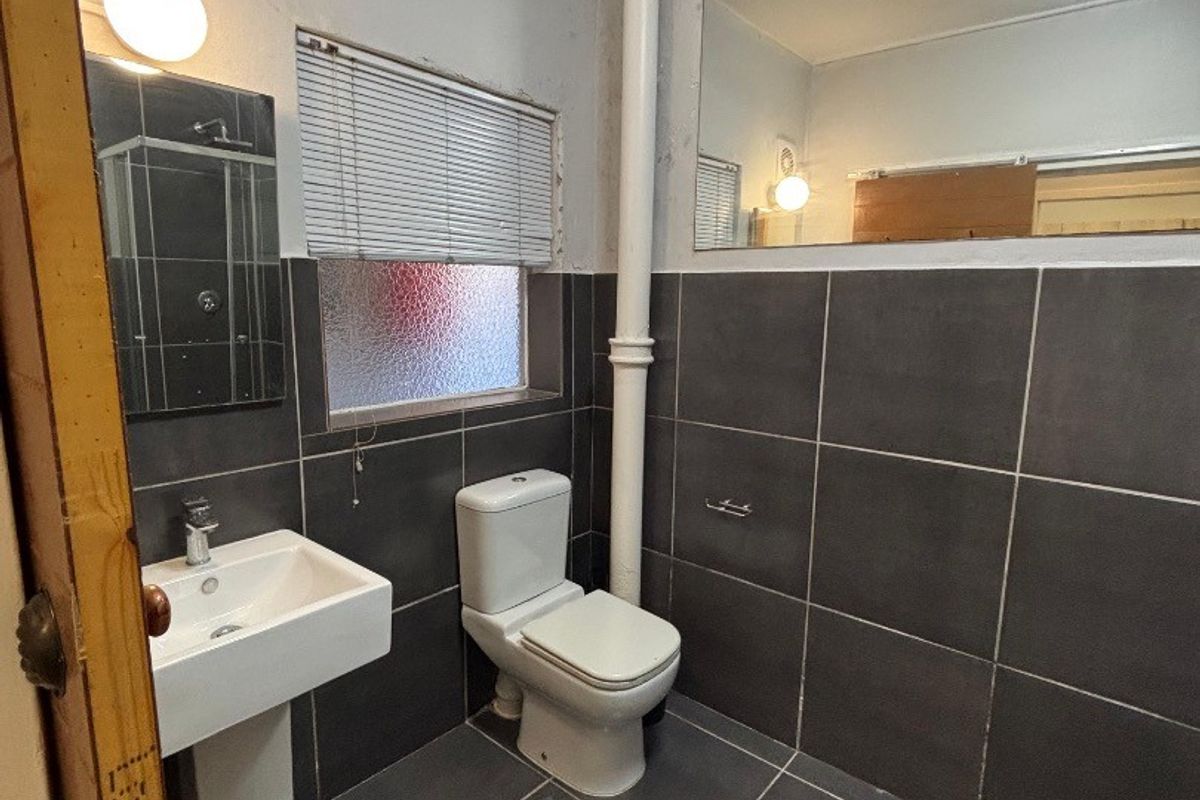 A functional bathroom featuring dark grey wall and floor tiles, a pedestal basin, toilet, and a large wall-mounted mirror.