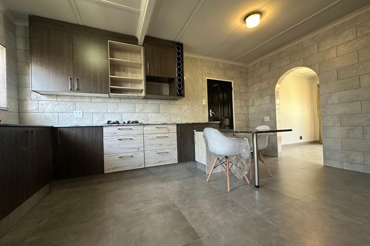Modern kitchen featuring dark and light wood-tone cabinetry, gas hob, tiled splashback, and large format floor tiles, leading through an archway to adjacent living space.
