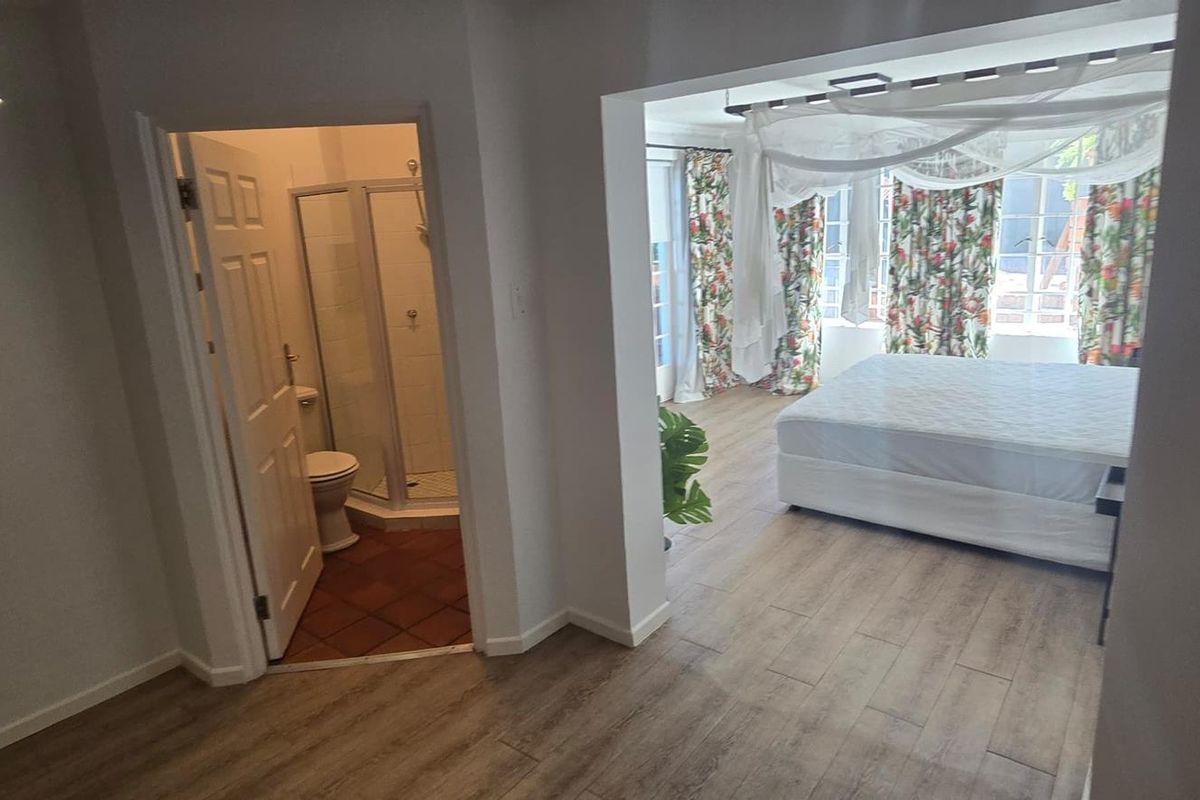 A bedroom featuring wood-look flooring and an en-suite bathroom with a shower and tiled floor, offering a functional and connected living space.