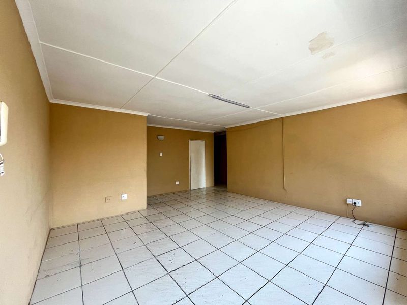 An empty living room featuring tiled flooring, neutral wall paint, and a ceiling light fixture, showing signs of wear and ceiling water damage.