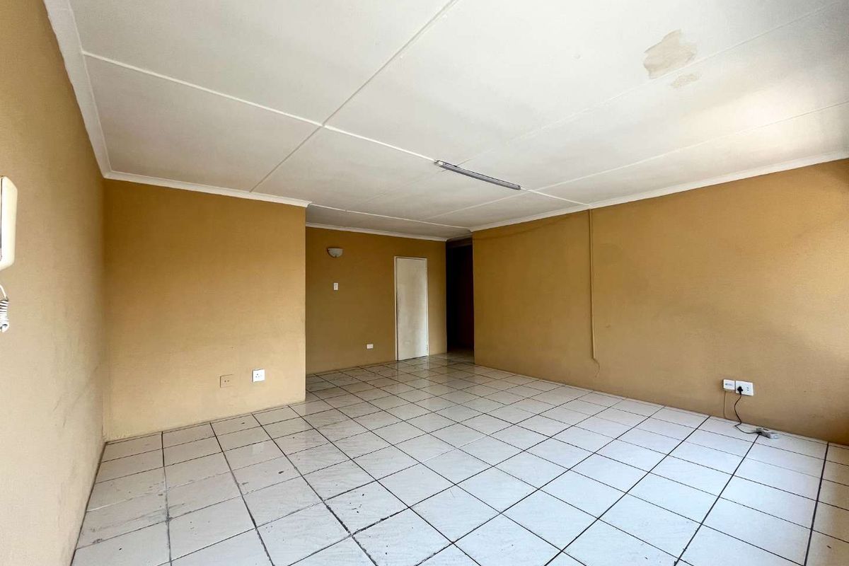 An empty living room featuring tiled flooring, neutral wall paint, and a ceiling light fixture, showing signs of wear and ceiling water damage.