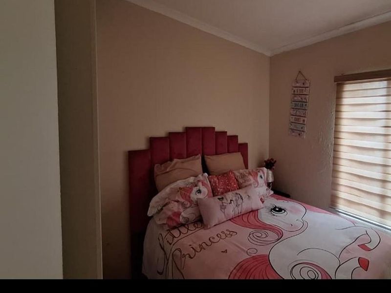 A bedroom featuring neutral wall paint and a window fitted with a roller blind.