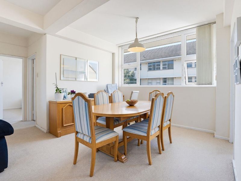 A bright dining room featuring neutral carpet flooring, a large window providing natural light, and a central pendant light fixture.