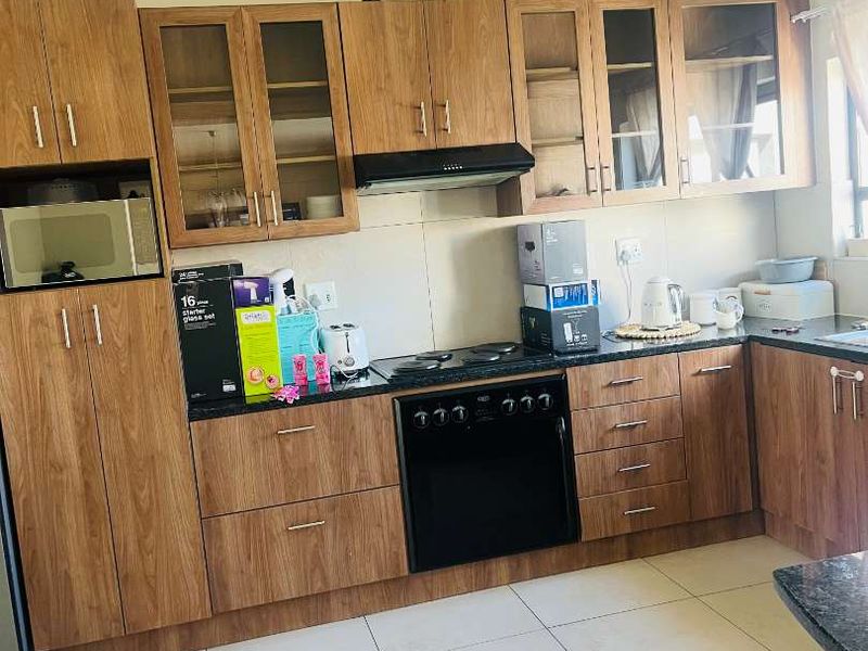 A functional kitchen featuring wood-finish cabinetry, dark countertops, integrated oven, hob, and extractor fan with neutral tiled flooring.