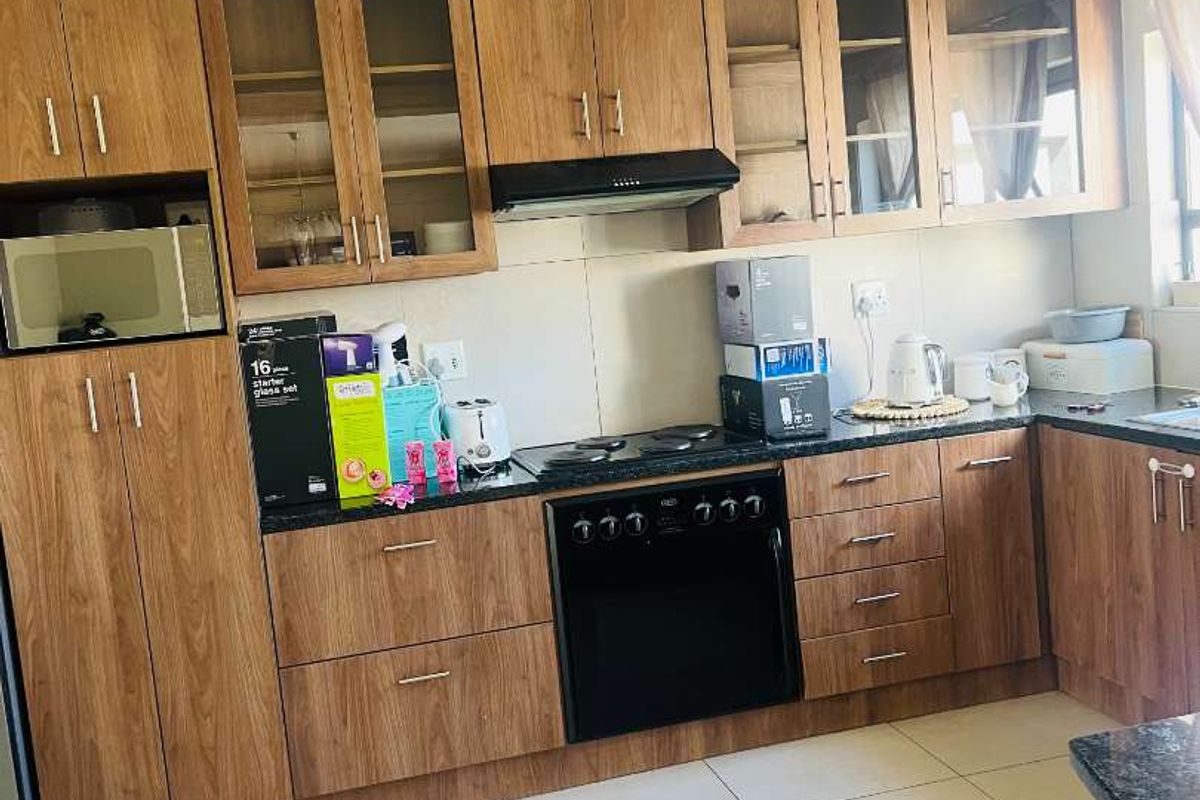 A functional kitchen featuring wood-finish cabinetry, dark countertops, integrated oven, hob, and extractor fan with neutral tiled flooring.