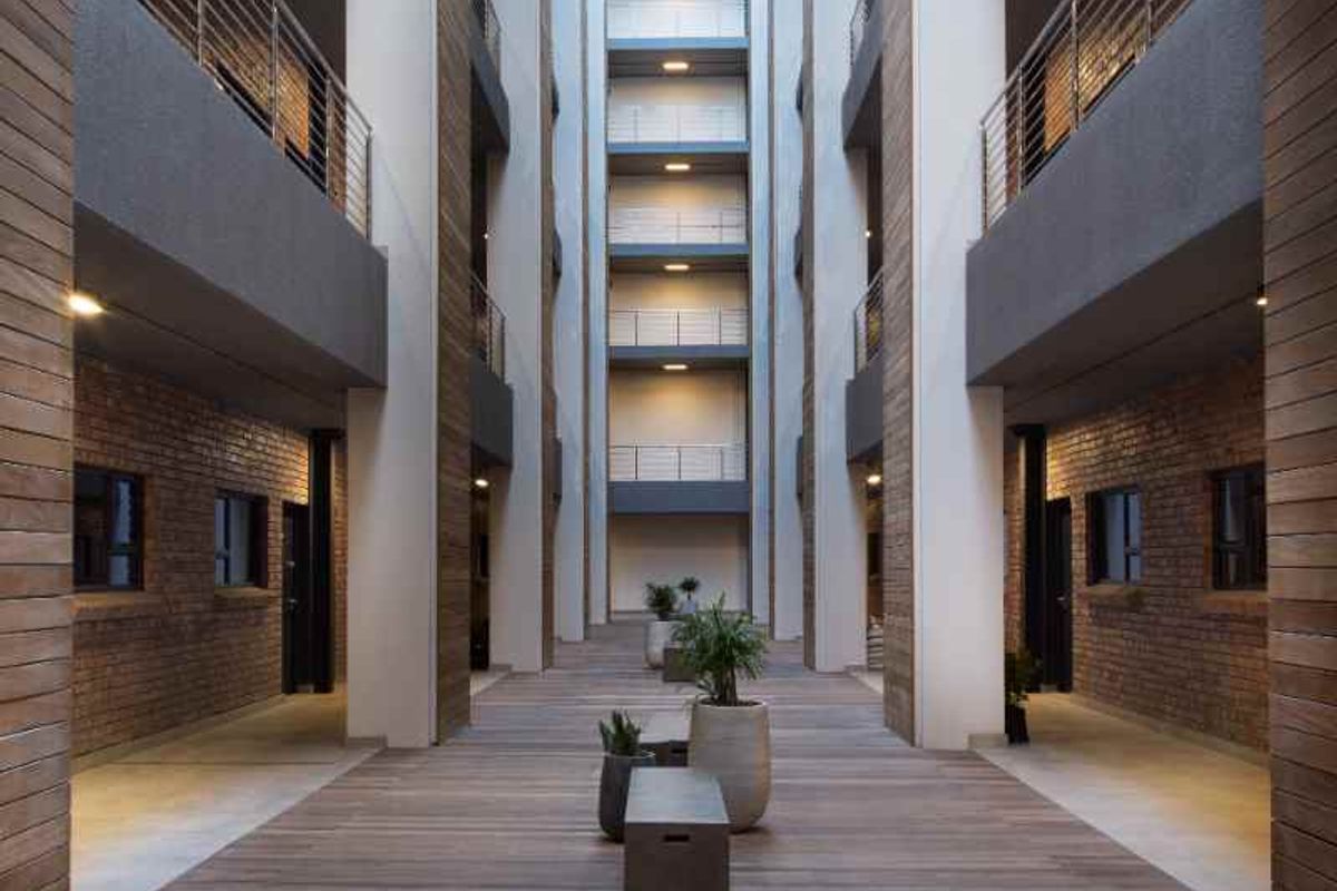 A modern apartment complex central courtyard featuring timber decking, exposed brick walls, and multi-level walkways with metal balustrades.