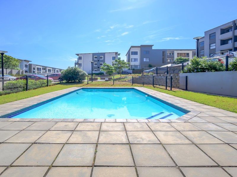 Communal swimming pool area featuring a paved deck, perimeter fencing, and landscaped surroundings within the apartment complex.