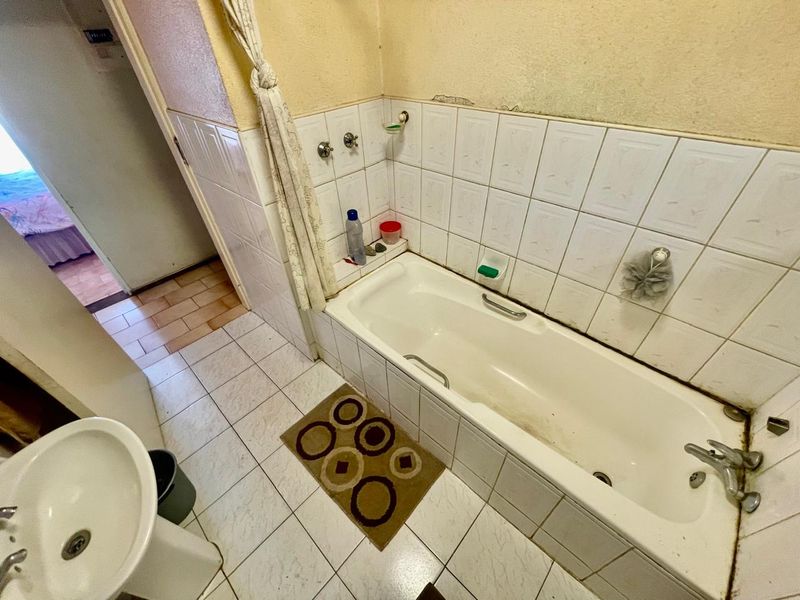 A dated bathroom featuring a standard bathtub, pedestal basin, and ceramic tiling, requiring cosmetic updates and maintenance to improve its overall condition.