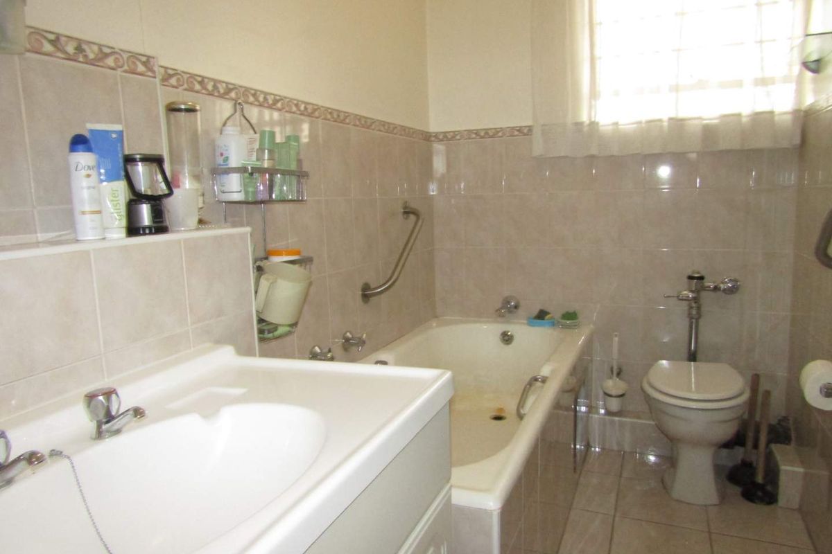 A functional bathroom featuring a built-in bathtub, wall-mounted grab rail, pedestal basin, and toilet with a flush valve system.