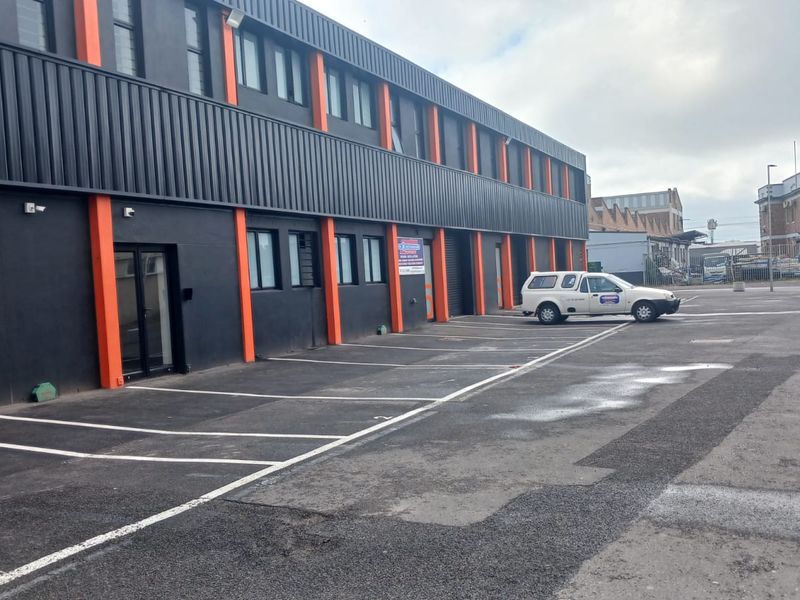 Industrial property exterior featuring a modern black and orange facade with dedicated asphalt parking bays and glass entrance access.