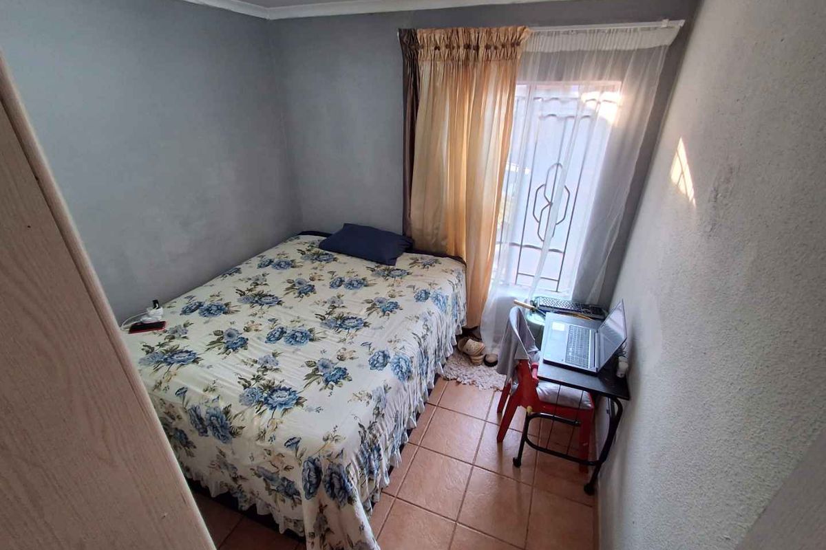 A compact bedroom featuring tiled flooring, a window with security bars, and neutral wall finishes.