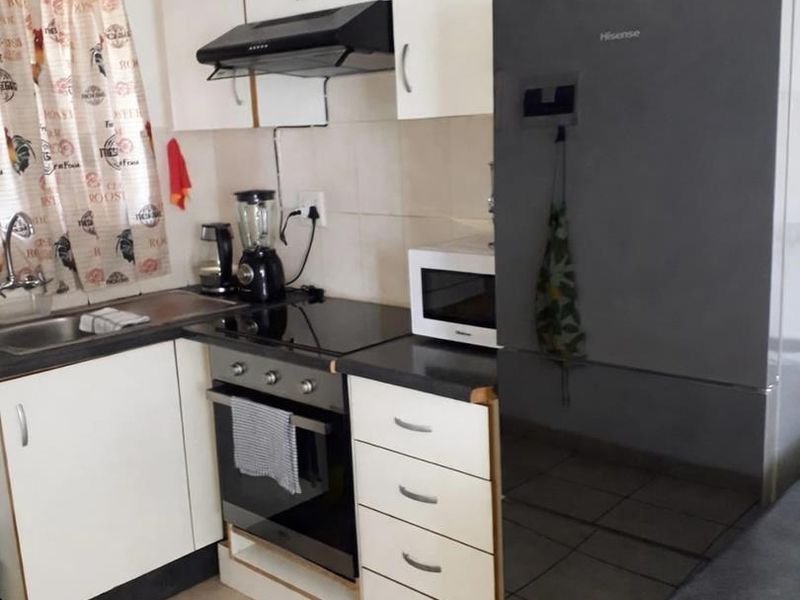 Compact kitchen featuring white cabinetry, dark laminate countertops, tiled backsplash, and integrated appliances including an electric hob and oven.