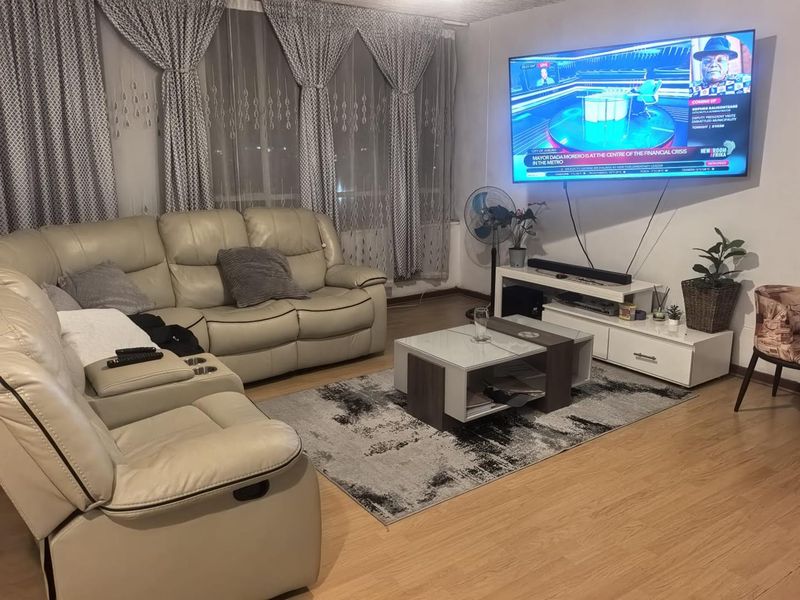 A comfortable living room featuring laminate flooring and large windows with curtain treatments, providing a functional space for relaxation and entertainment.