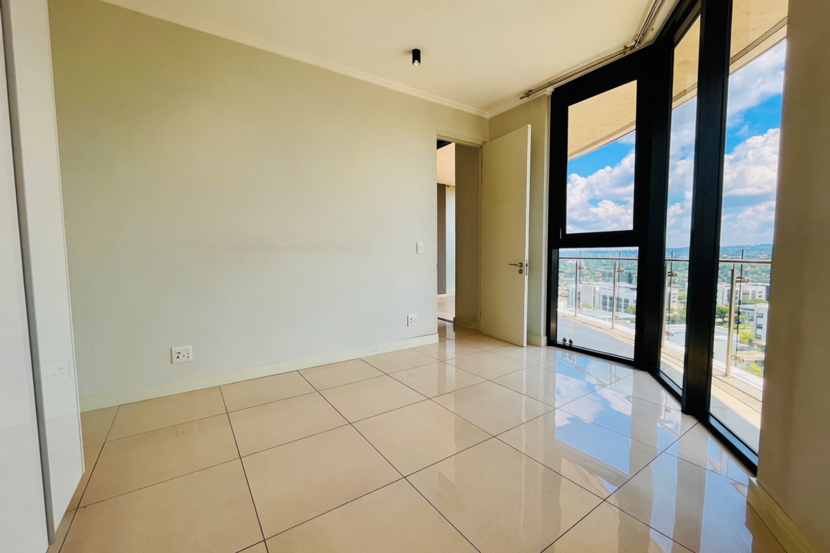 A bright, empty bedroom featuring large floor-to-ceiling windows with balcony access, polished tile flooring, and modern recessed ceiling lighting.