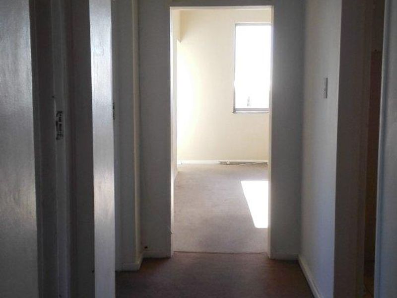 A vacant apartment hallway featuring carpeted flooring and transom windows, leading into an adjacent room with natural light.