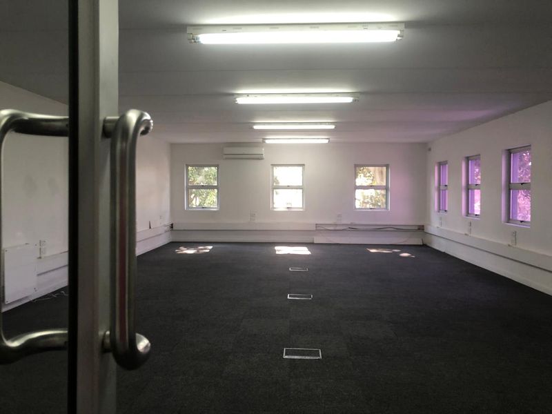 A spacious, empty open-plan office area featuring carpeted flooring, integrated floor power outlets, fluorescent lighting, and split-system air conditioning.