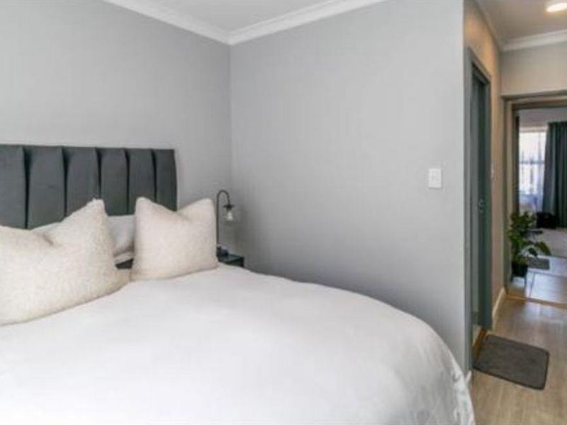 A well-maintained bedroom featuring neutral grey walls, coving, and built-in storage, with a view leading into an adjacent room.