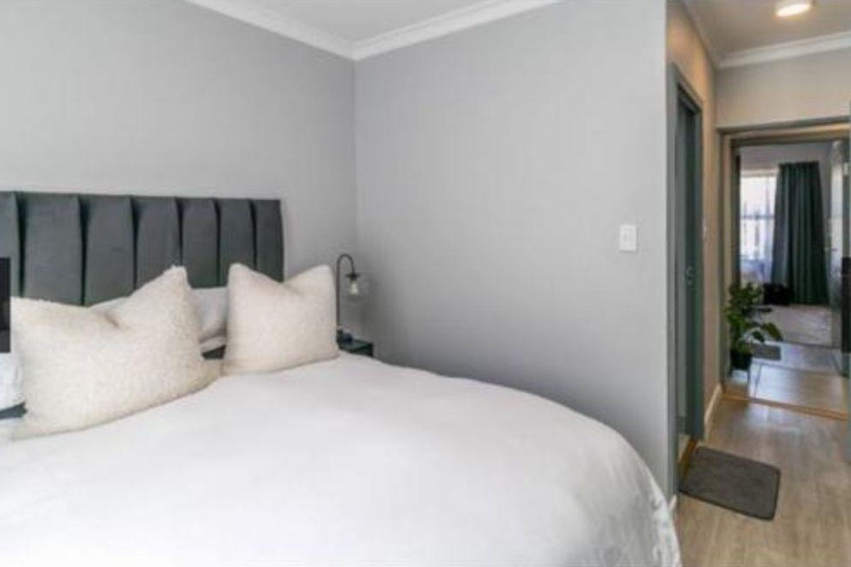 A well-maintained bedroom featuring neutral grey walls, coving, and built-in storage, with a view leading into an adjacent room.