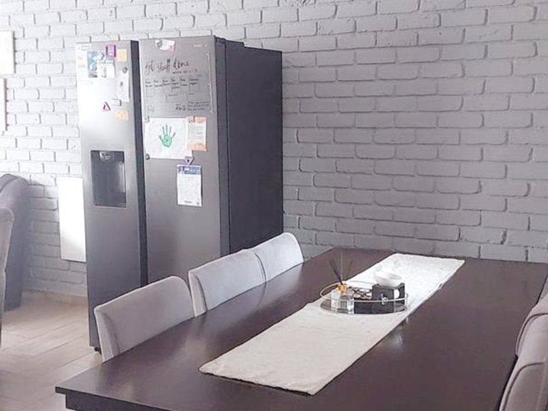 Dining area featuring a painted grey brick feature wall, neutral tiled flooring, and a modern ceiling light fixture.