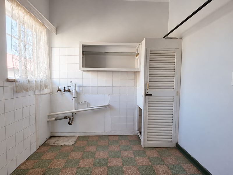 A functional laundry room featuring tiled splashbacks, built-in storage cabinetry, and exposed plumbing connections, ready for modernization.