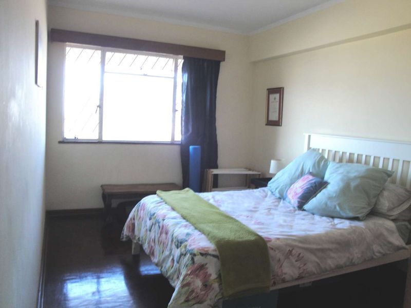 A standard bedroom featuring timber flooring and a window with security bars, offering a functional space with neutral wall finishes.